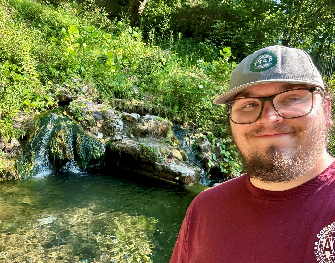 Jacob Martin stands in front of a mossy, rocky hill with rippling water in the background