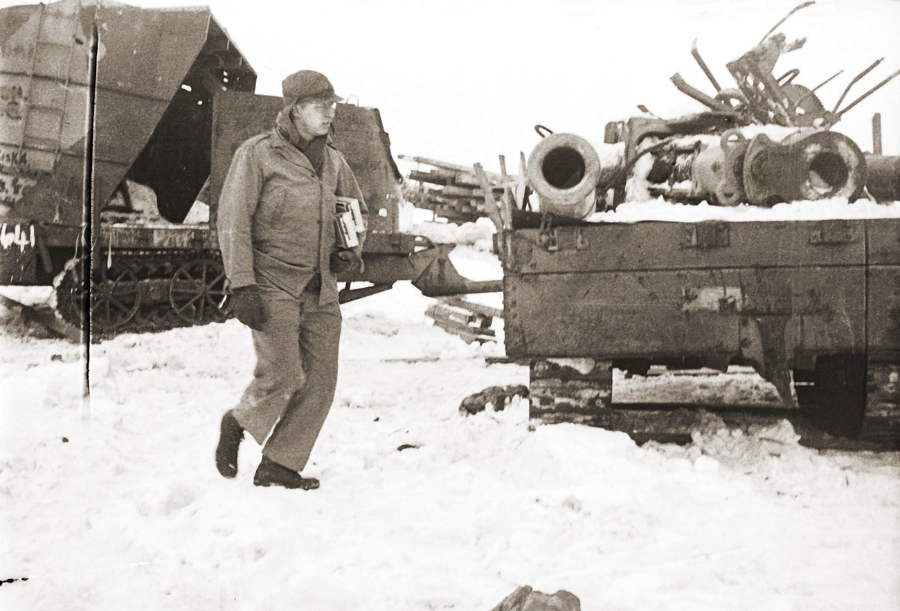 Man in uniform walking through snow towards cart full of dismantled large guns