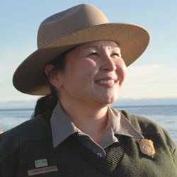 Picture of Jeanette Koelsch outside from the shoulders up with ocean in the background in a park ranger uniform.