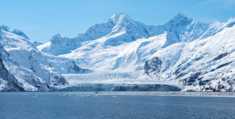 A tidewater glacier meets the sea from the mountains.