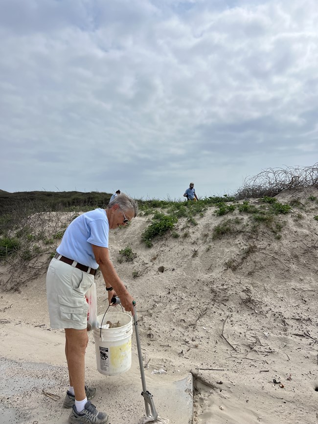 A person picking up trash on the beach.