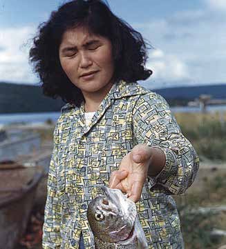A woman with eyes closed extends her arm, holding a silver fish under the gills