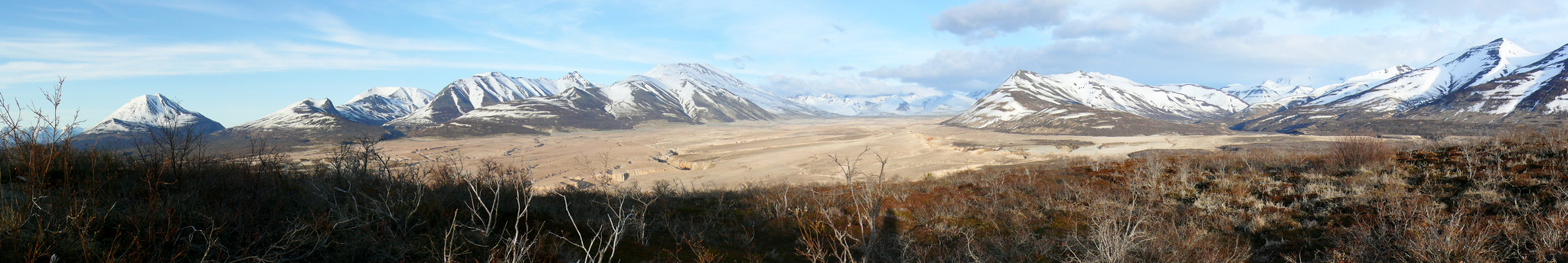 Panorama of an expansive volcanic valley, framed by snow covered mountains and low vegetation