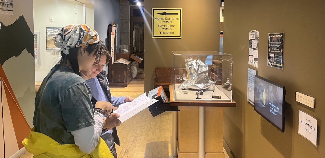 Two individuals exploring a display of artifacts while completing junior ranger activities in a museum environment.