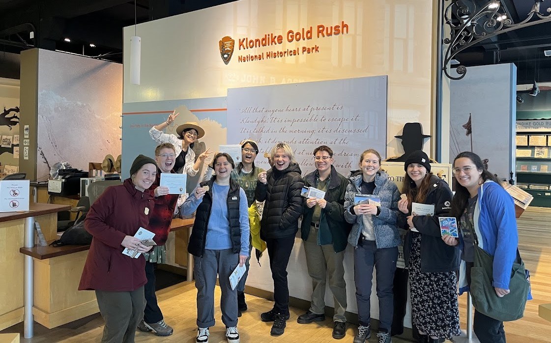 Community Volunteer Ambassadors and a park guide pose for a photo at the Visitor Center after their junior ranger swearing-in ceremony.