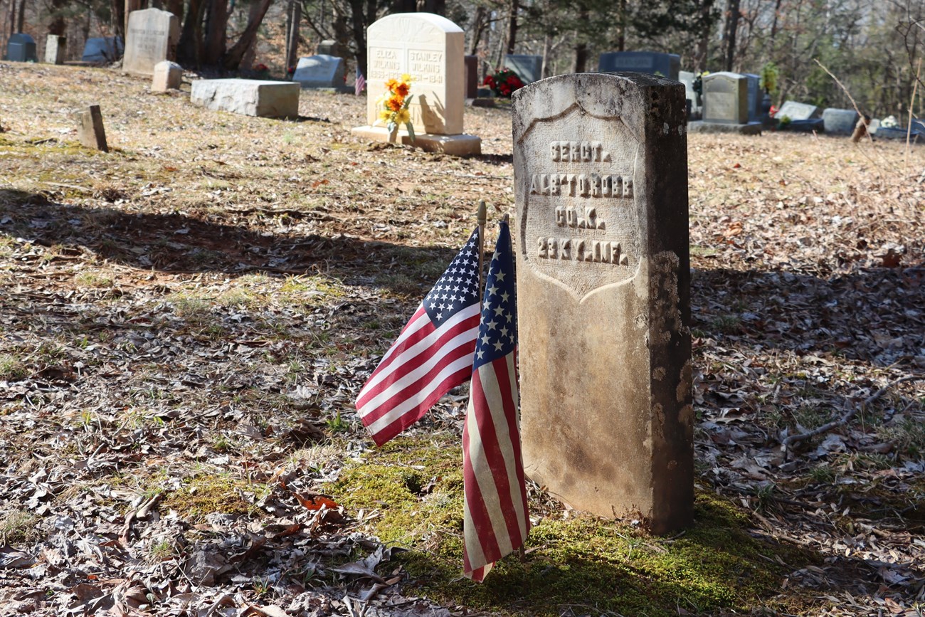 A tombstone with military insignia and American flags posted near it.