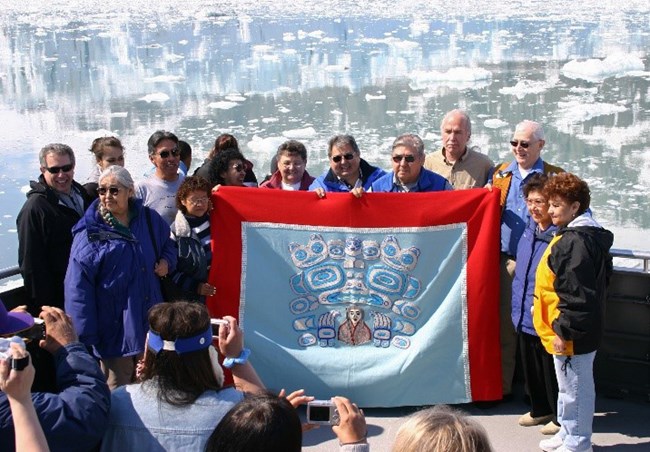 A group of Tlingit elders pose with a traditional blanket in front of a glacier