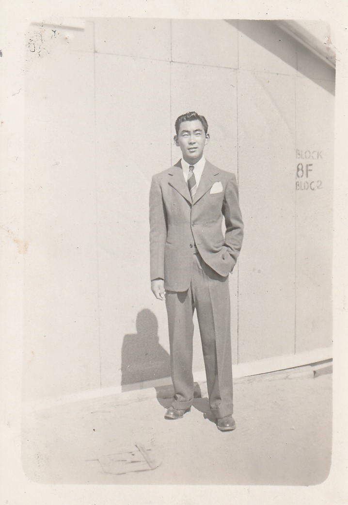Young man in a suit standing in front of a building with the label "block 8f bldg 2"