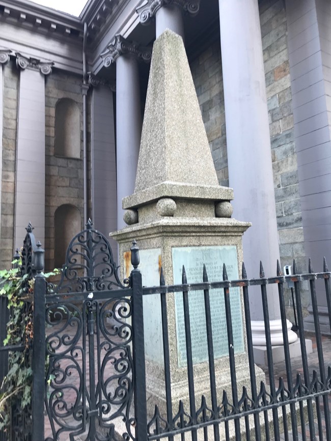 a granite pointed obelisk with a square based that has metal engravings on all sides.