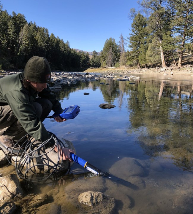 A scientist holding a piece of equipment that is submerged in river water.