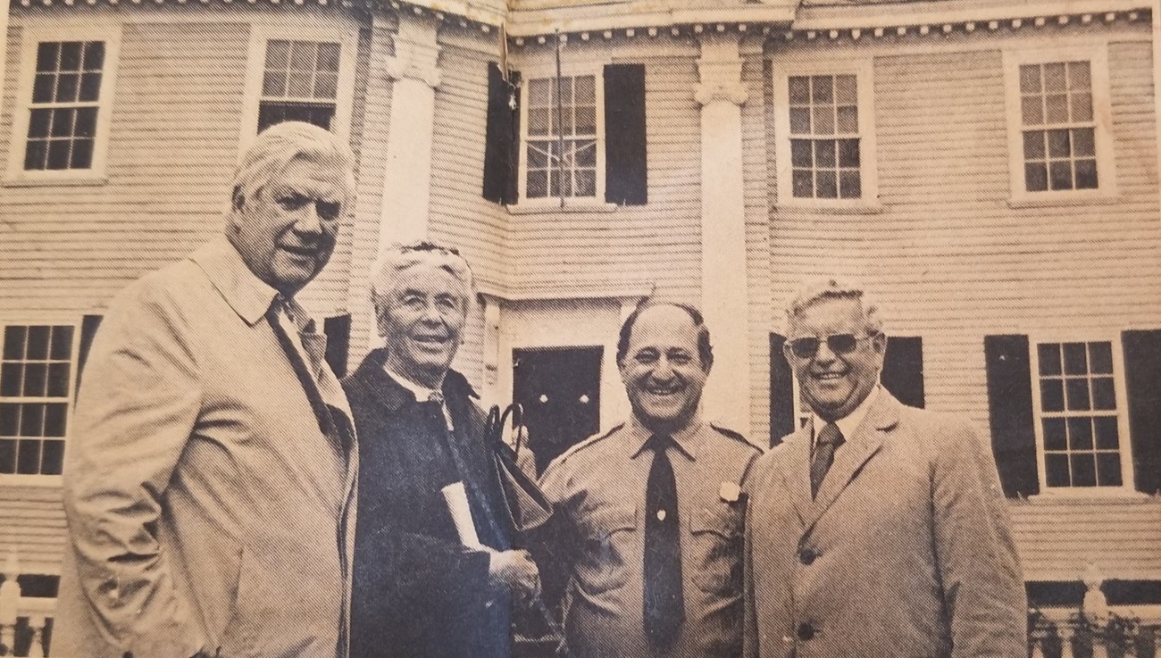 Newspaper image of four people posed in front of Longfellow House