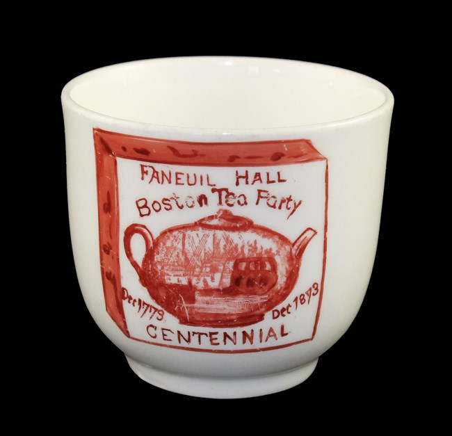 White teacup with red printed decoration of a teapot and ship captioned Boston Tea Party Centennial