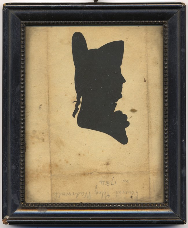 Silhouette of man wearing tall military hat.