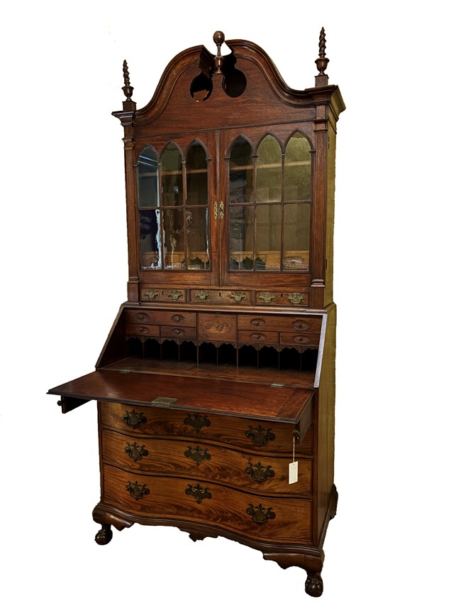Dark wooden desk with lower drawers, fold-out desk top, and top section with glass-fronted bookcase