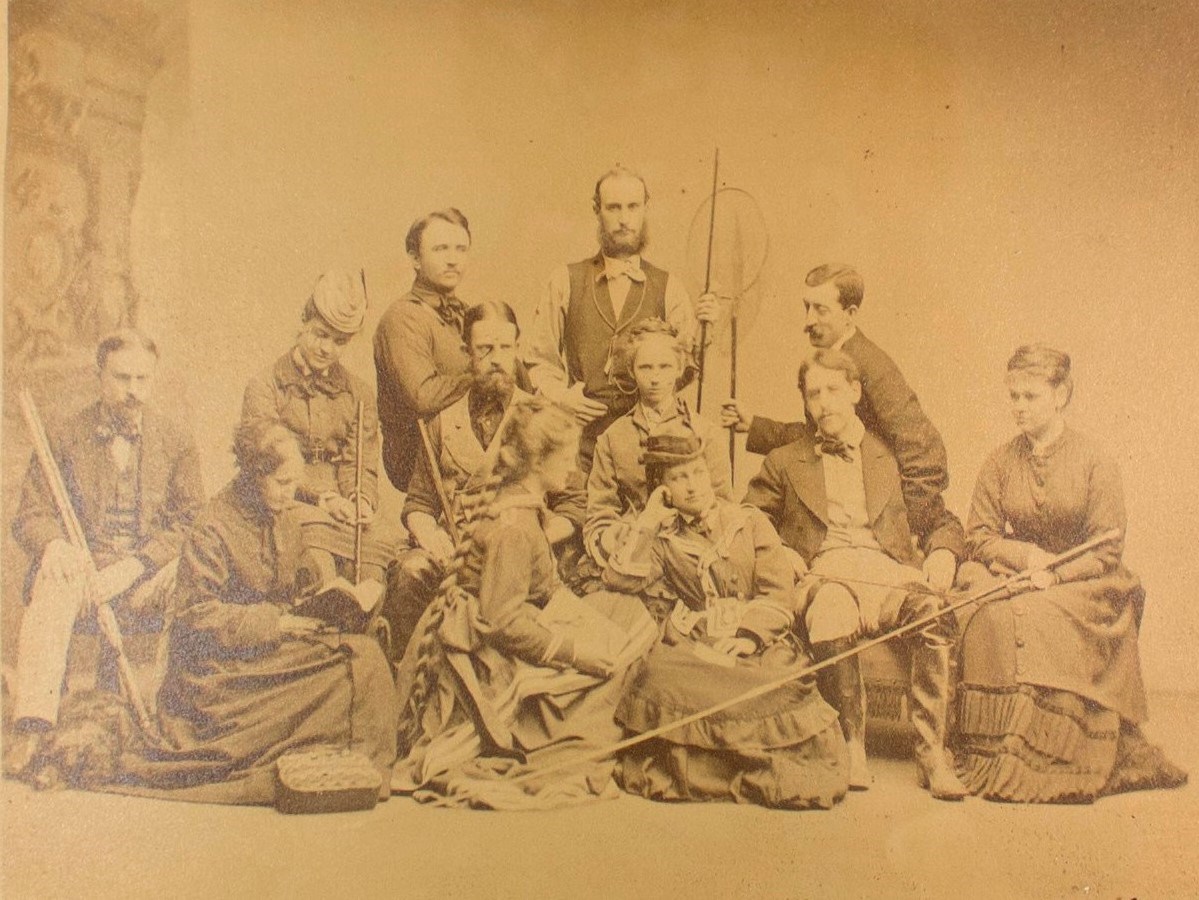 Studio portrait of 12 men and women with fishing and hunting gear in formal clothing.