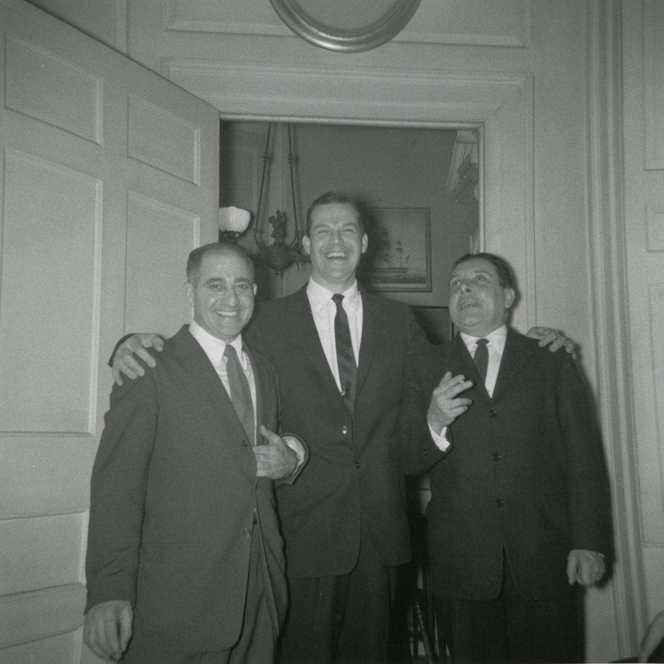 Black and white photograph of three men in suits in front of doorway