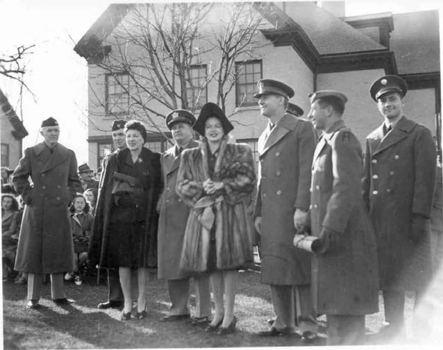 a young woman in a fur coat stands surrounded by military personel