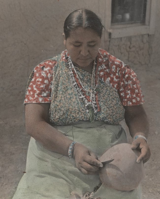 Legoria Tafoya sits outside looking down at the pot in her lap with a knife in one hand