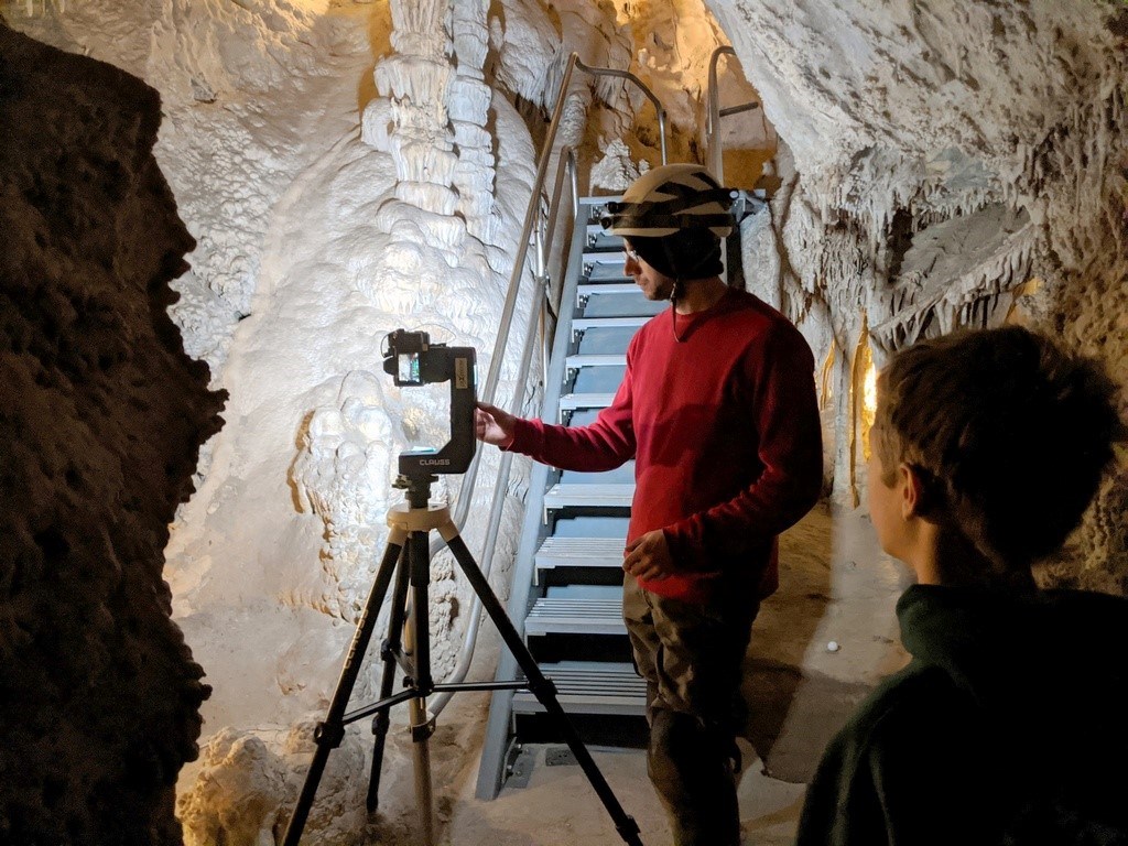 Person operating a small camera mounted on a specialized tripod head in front of a stairway deep inside of Lehman Caves.