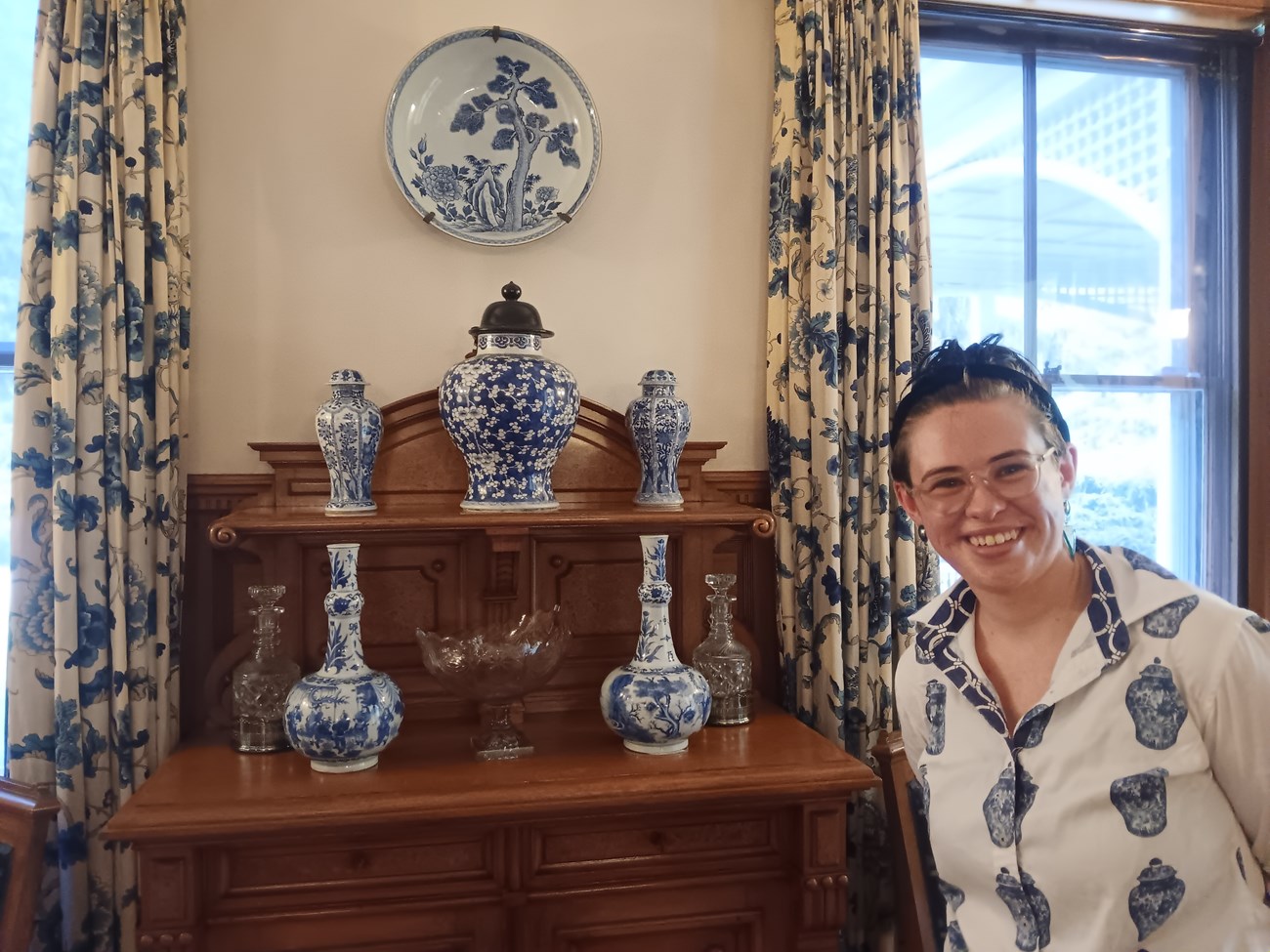 curator posing with ceramics in the Marsh-Billings-Rockefeller mansion wearing a blue and white shirt that matches the ceramics