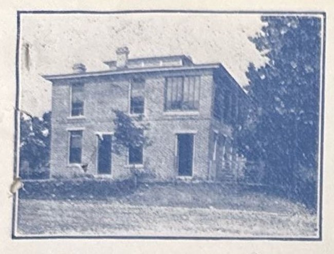 Photo of a two-story square building with large windows. There are trees larger than the building on the right side of the building.