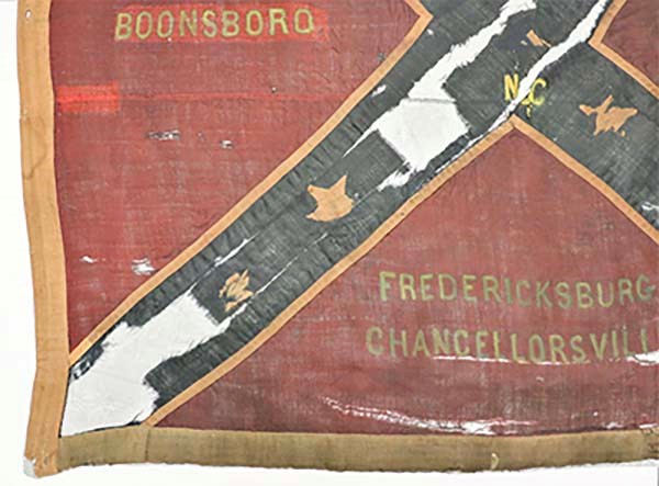 The bottom left corner of a battle flag with red fabric outlined in white fabric and intersected by a blue fabric X with stars on it, the words "Boonsboro, Fredericksburg and Chancellorsville" are seen.