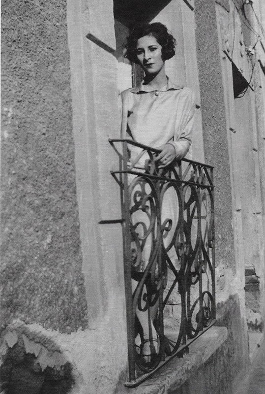 Luisa Moreno leans against a wrought iron railing on the balcony of a stucco building