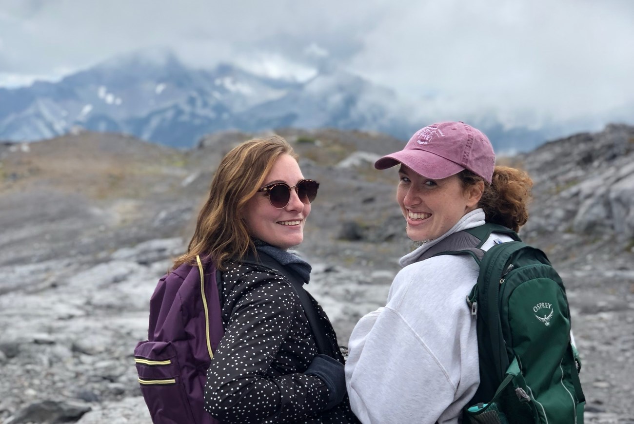 Two visitors smiling for the camera with a mountain in the distance