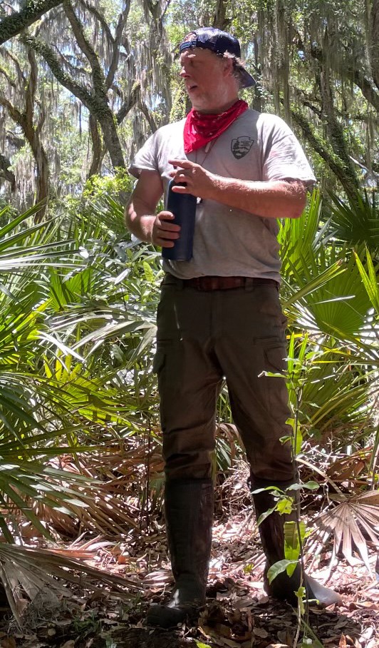 Man with hat on backward standing in trees