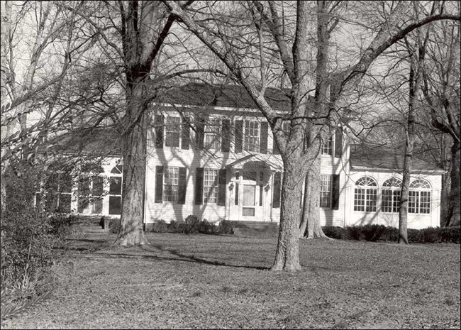 White 2-story house with attached 1-story wings on each side. 15 windows cover front of house.