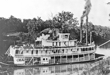 A black and white photo of a large steamboat with steam.