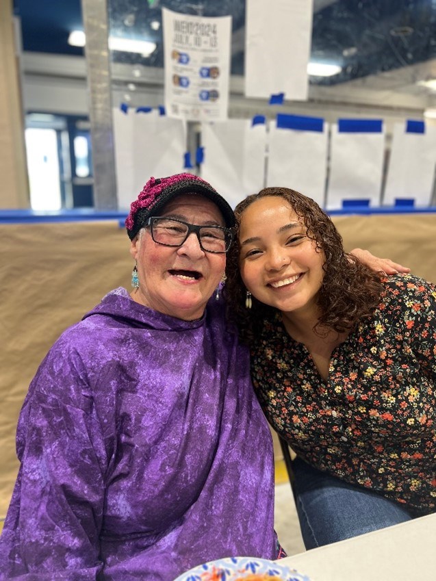 an old woman in bright purple smiles and embraces a young women wearing a floral kaspbak.