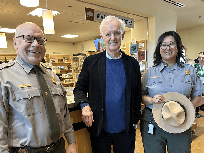 Two people in park ranger uniforms pose with a man in a visitors center