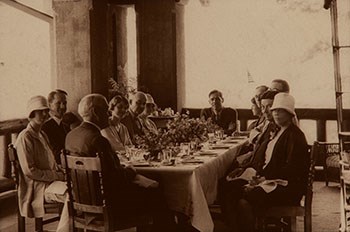 A long table is filled with dishes and food is surrounded by people dressed up for a celebration.