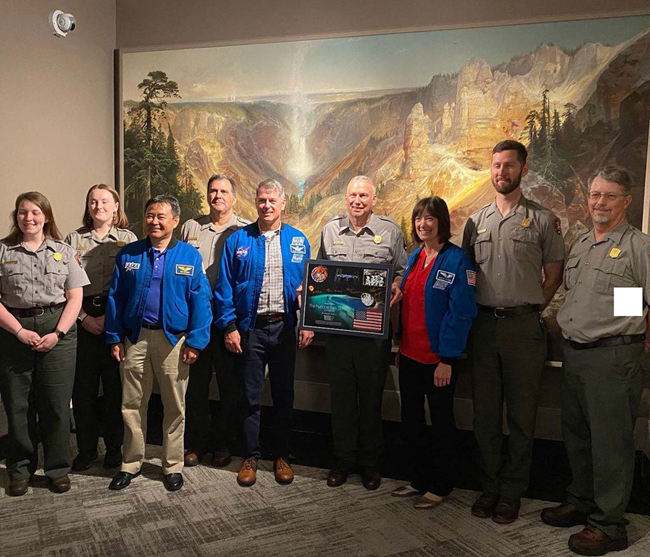 Several astronauts and park rangers pose in front of a large colorful painting of the Grand Canyon.
