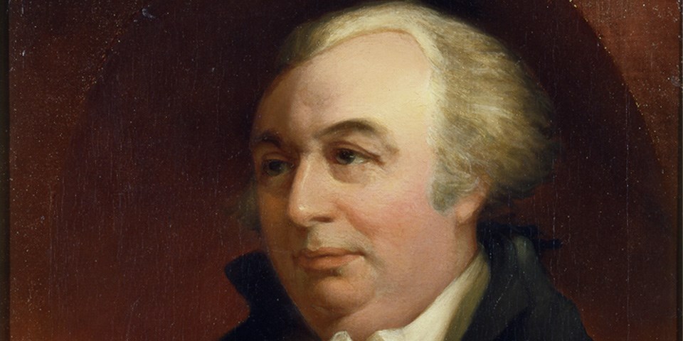 Morris wearing a black coat with hair pulled back against red backdrop