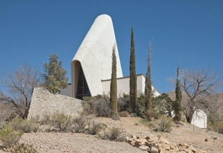 A modernist church with a unique curved roof with angular walls in a desert landscape.