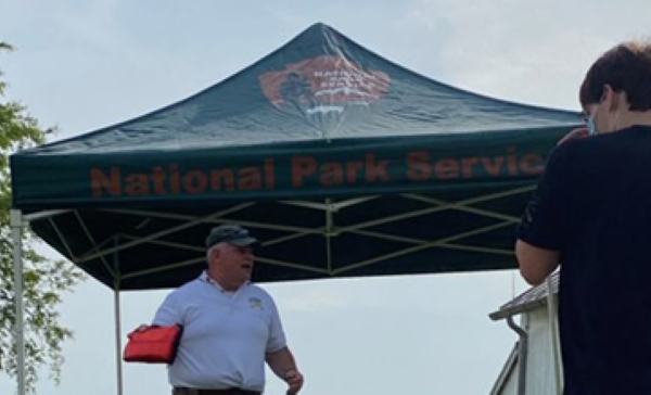 A photograph of a man in a polo shirt and a ball cap under a canopy outdoors.