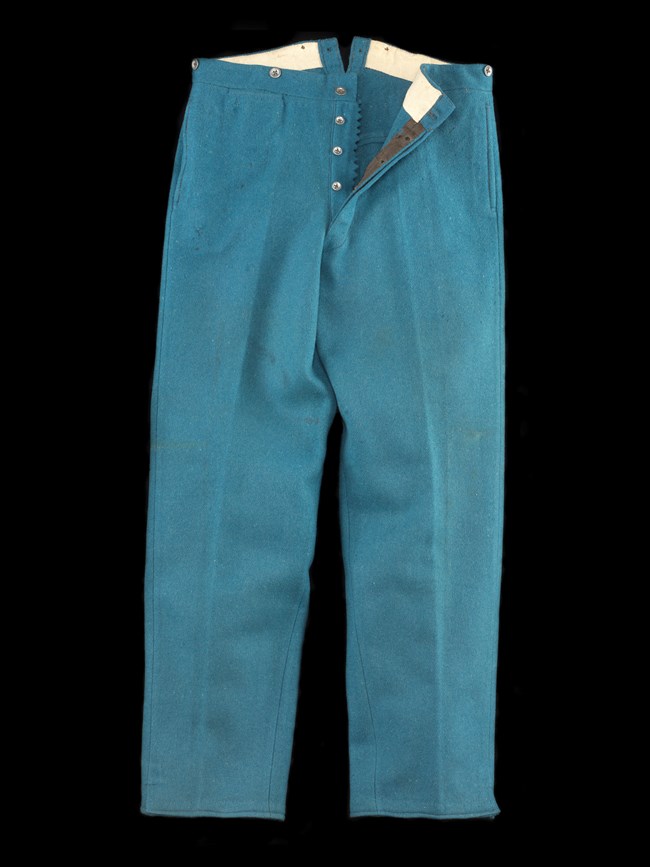 A pair of blue trousers against a black background. The buttons are unbuttoned, and the right side is folded over