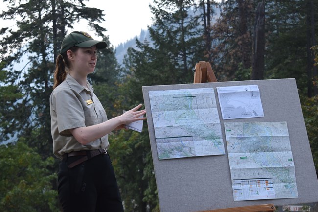 Volunteer Sarah talks next to an easel displaying maps