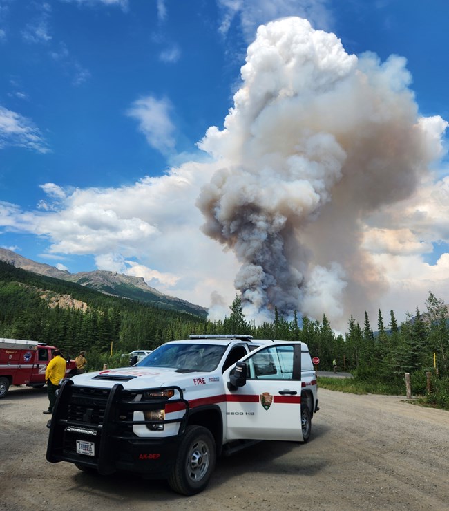 A National Park Service fire truck parked with smoke rising in the background