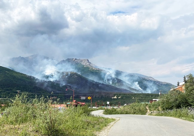 Smoke from a wildfire rises in a valley with several buildings nearby