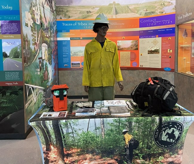 A museum area with a table display about wildland fire, and a mannequin in fire gear behind it.
