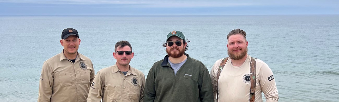 Four men stand in front of large body of water.