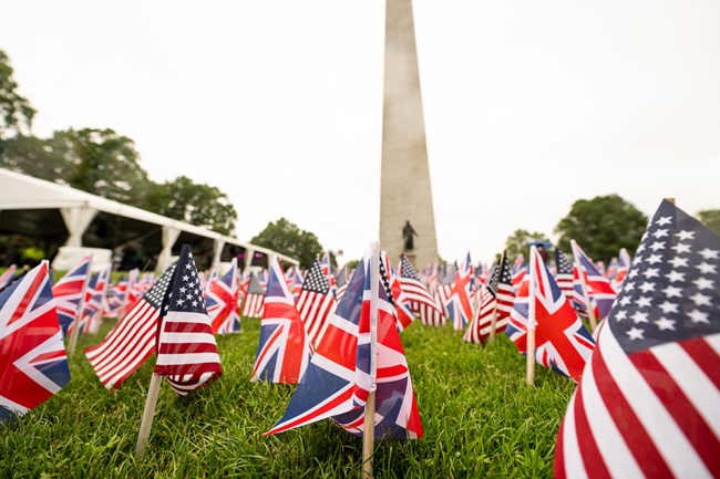 lines of US and UK flags in front of the Bunker Hill Monument