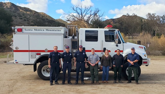 A group of people stands in front of a fire engine in an outdoor setting