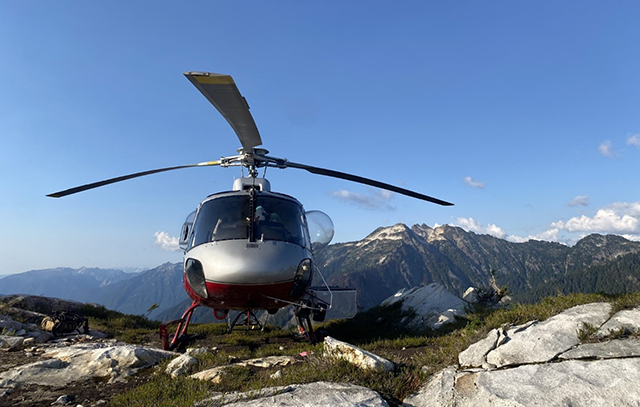 A helicopter landed in a rocky field with mountains in the background