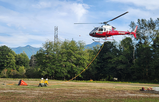 Two women on the ground adjust a line attached to a hovering helicopter
