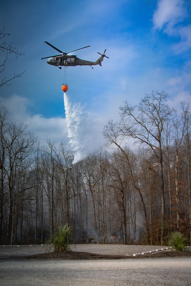 A helicopter drops water from a bucket suspended below it