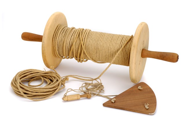 A spool of rope with a triangular piece of wood tied to the rope's end.